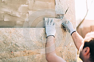 Worker installing stone tiles on wall on construction site