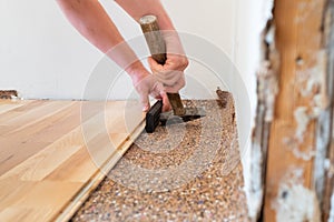 Worker installing wood parquet board during flooring work with hammer