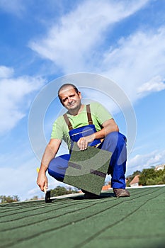 Worker installs bitumen roof shingles