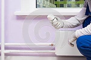A worker installs a heating regulator on a radiator