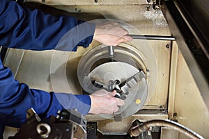 The worker installs a new metal part in the chuck spindles for processing on the CNC machine. Hands of the worker close