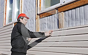 A worker installs panels beige siding on the facade