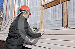 A worker installs panels beige siding on the facade