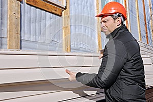 A worker installs panels beige siding on the facade