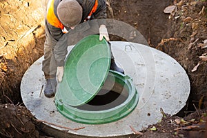 A worker installs a sewer manhole on a septic tank made of concrete rings. Construction of sewerage networks for country