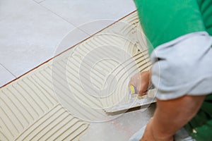 Worker installs tiles on the floor. He put glue using comb trowel.