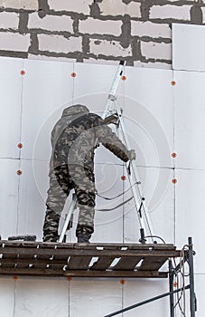 Worker insulates the walls of the house with plastic panels