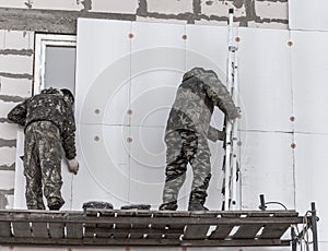 Worker insulates the walls of the house with plastic panels