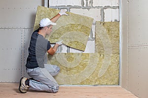 Worker insulating a room wall with mineral rock wool thermal insulation