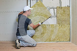 Worker insulating a room wall with mineral rock wool thermal insulation