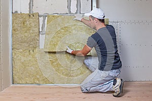 Worker insulating a room wall with mineral rock wool thermal insulation