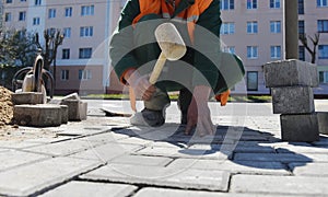 A worker knocks a hammer on the paving slabs.