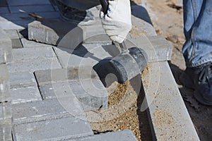 A worker knocks on paving slabs with a construction hammer.