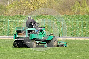 Worker on a large green lawn mower mows the grass on the football field. Landscape design and maintenance of green areas of the