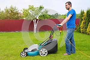 Worker with a lawn mower mows grass in the garden. Side view