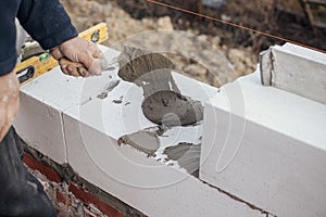 Worker laying autoclaved aerated concrete blocks, working with adhesive and trowel. Builder installing masonry white blocks close