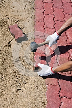 Worker laying red concrete paving blocks.