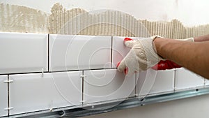 A worker lays and installs white ceramic tiles in a kitchen. Ceramic tile-fish. Laying ceramic tiles on the backsplash