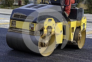 Worker leads the vibrating road roller to compact the asphalt