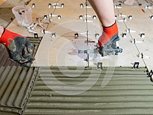 A worker is leveling the ceramic tile with wedges and clips. Tile leveling system