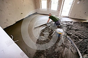 Worker is leveling floor screed over floor heating system in residential building under construction