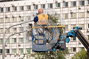 Worker in lift bucket during installation of metal pole with street lamp, street light pole with double head