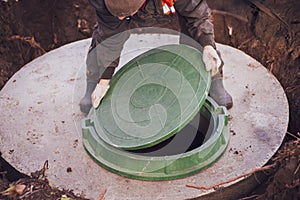 A worker lifts the manhole cover of a sewer well. Construction and maintenance of septic tanks in the village