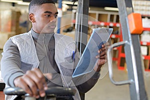 Worker in logistics warehouse using forklift checking list