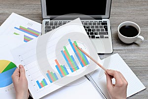 Worker looking at graphics. Top view on hands holding graphs, laptop, cup of coffee, workplace workstation, project progress best