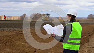 The worker looks at the drawings on the background of the road under construction.