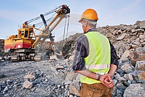 Worker looks on excavator works at opencast