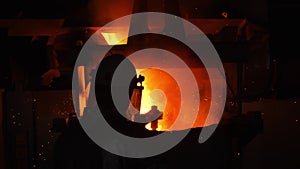 Worker looks at pouring hot liquid metal in dark workshop