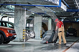 Worker with machine cleaning floor in parking garage.