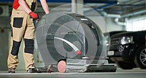 Worker with machine cleaning floor in parking garage.