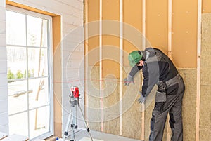 The worker makes finishing works of walls with a white wooden board, using laser line level. Building heat-insulating