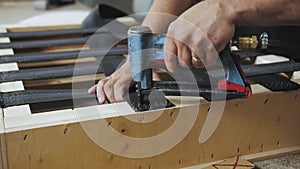 A worker makes a sofa in a furniture factory. Close-up of a carpenter working with a pneumatic pistol, slow motion.