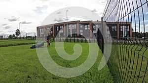 Worker man cutting grass lawn in private townhouse yard on cloudy day. Time-lapse