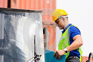 Worker man in hard hat and safety vest standing on container stackers control loading containers box from cargo