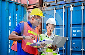 Worker man in hardhat and safety vest holding clipboard checklist and Female foreman using laptop control loading containers box