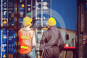 Worker man in hardhat and safety vest holding laptop and Female engineer control loading containers box from cargo