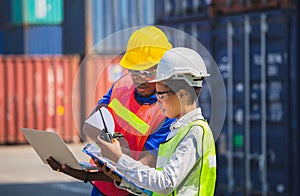 Worker man in hardhat and safety vest holding laptop and Female foreman talks on two-way radio control loading containers box from