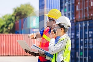 Worker man in hardhat and safety vest holding laptop and Female foreman talks on two-way radio control loading containers box from