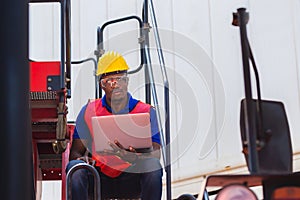 Worker man in hardhat and safety vest holding laptop standing on container stackers control loading containers box from cargo