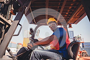 Worker man in hardhat and safety vest sitting in container stackers control loading containers box from cargo