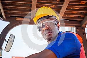 Worker man in hardhat and safety vest sitting in container stackers control loading containers box from cargo