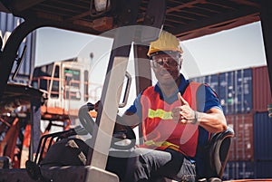 Worker man in hardhat and safety vest sitting in container stackers smiling with giving thumbs up as sign of Success