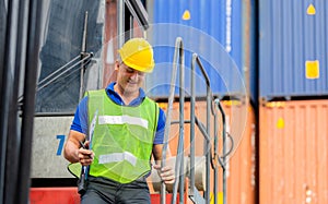 Worker man in hardhat and safety vest standing on container stackers control loading containers box from cargo