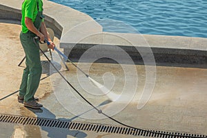 Worker man in uniform washes street or park sidewalk near water pool or fountain. Municipal service of city cleaning process. Guy