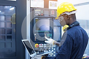 Worker man with yellow helmet and ear protection typing keyboard of laptop computer at factory