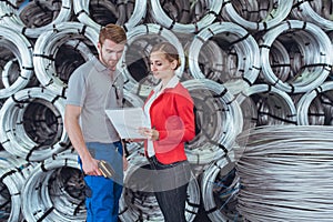 Worker and manager discussing inventory list of materials in warehouse